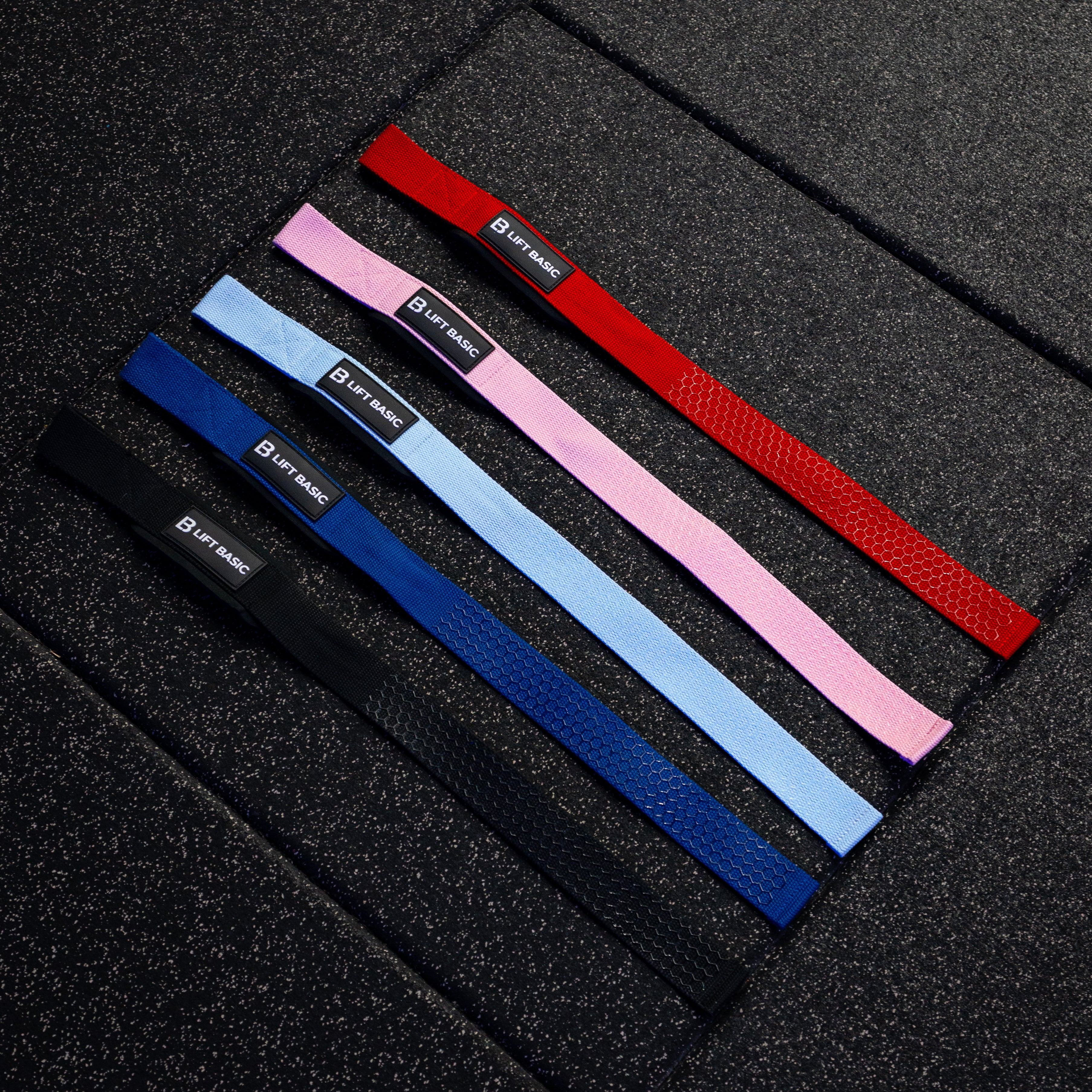 Set of lifting straps in red, blue, pink, and black on a textured black surface.