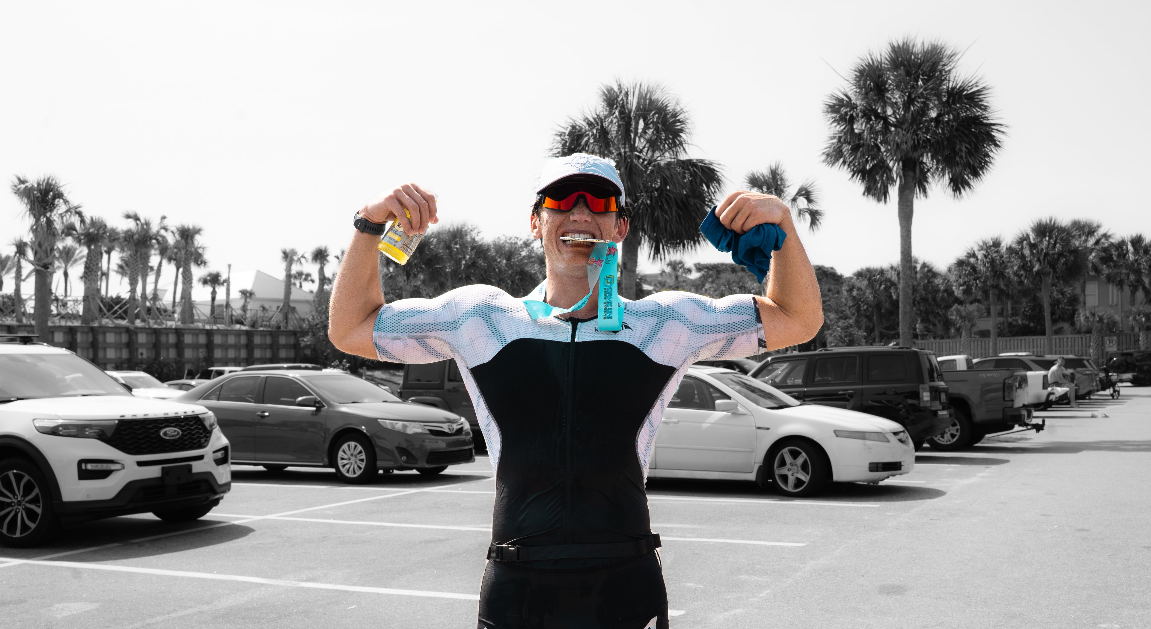 Person in cycling gear holding a water bottle in a parking lot with palm trees in the background